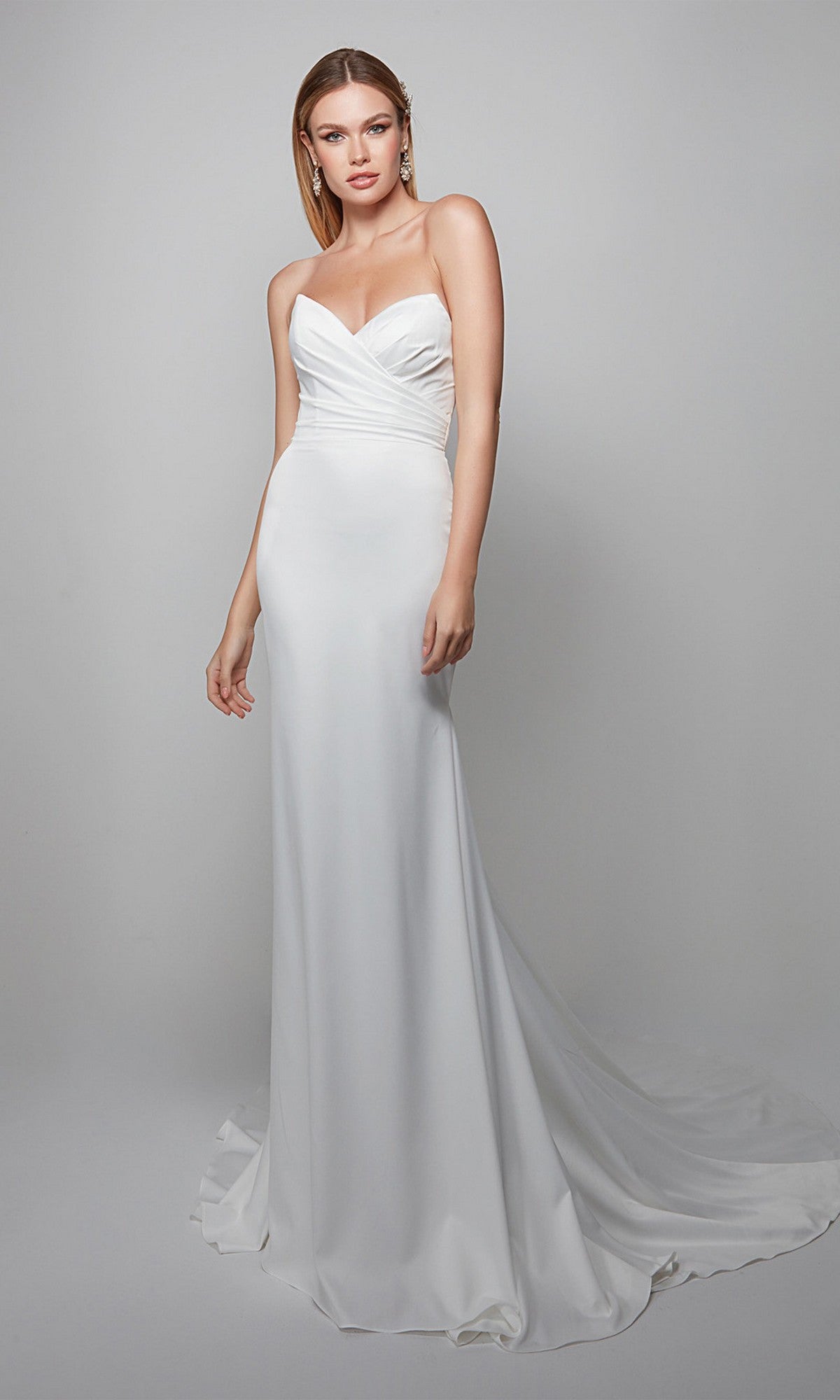 A woman wears the Alyce 7056 long formal dress, a strapless white gown with a sweetheart neckline, fitted bodice, and flowing train, set against a plain gray background.
